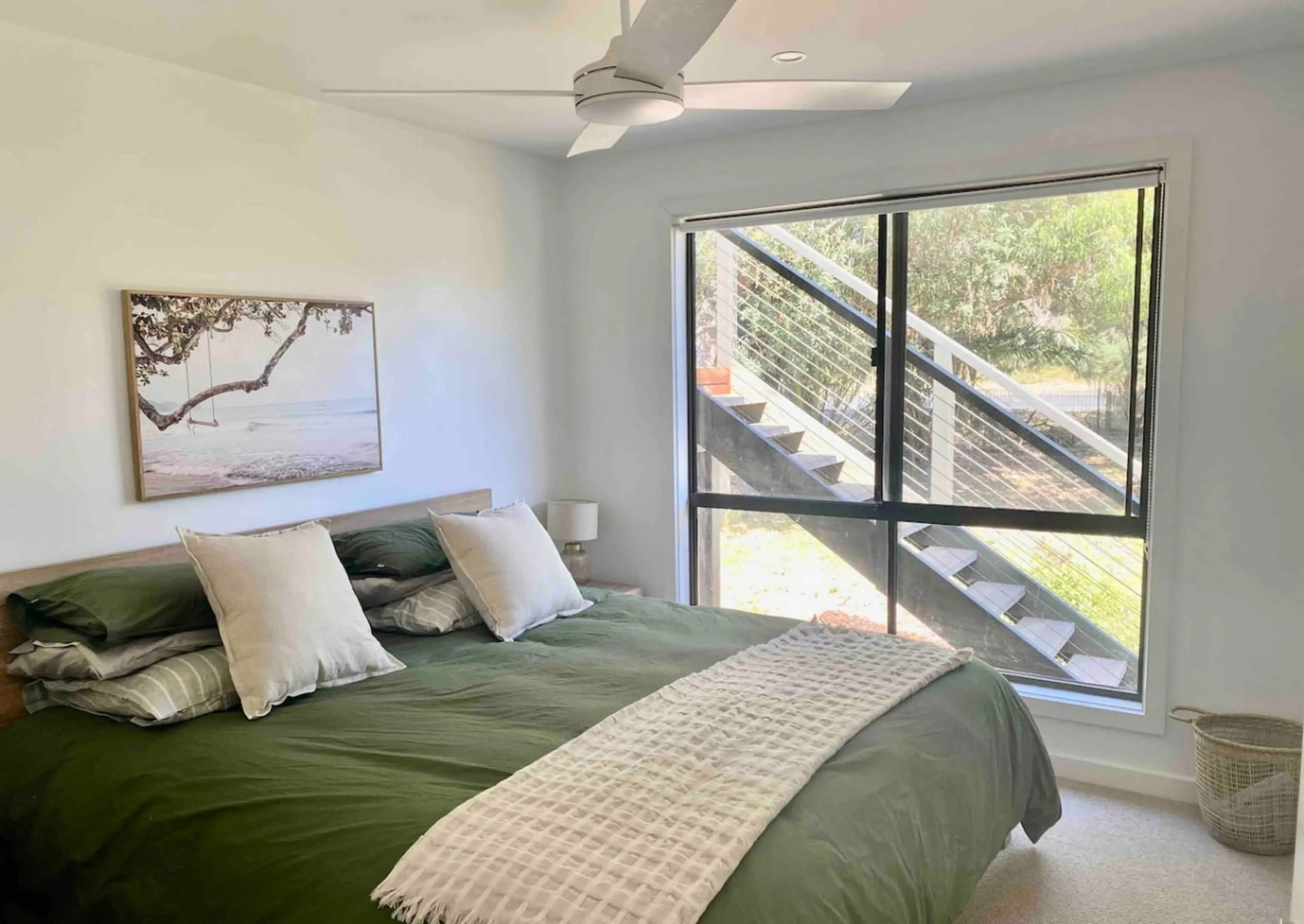 Master bedroom with king bed, green linen and coastal artwork